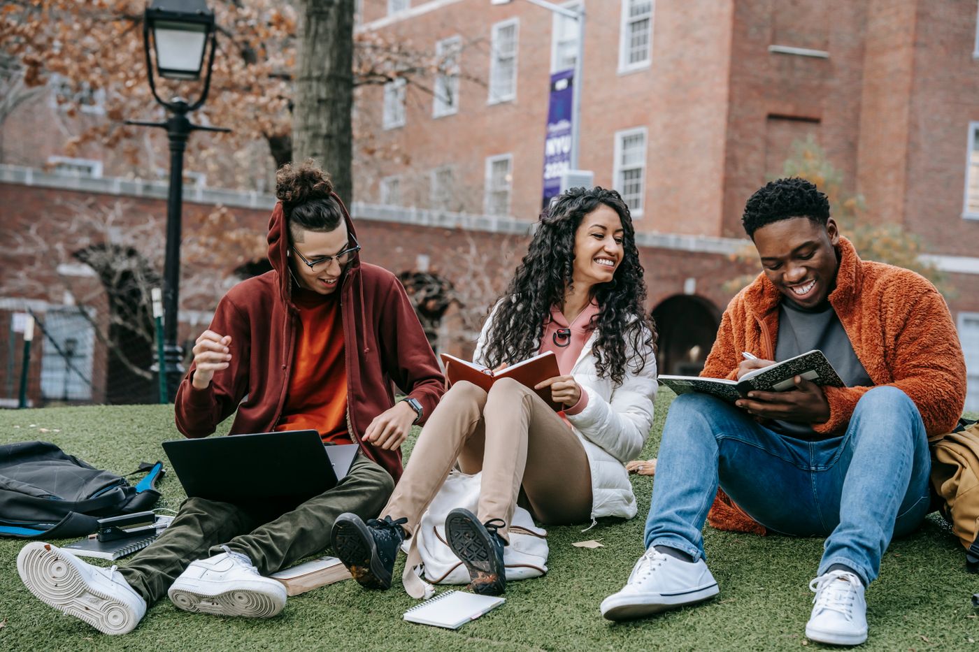 Three young students working on their project together, laughing over their notebooks and laptop